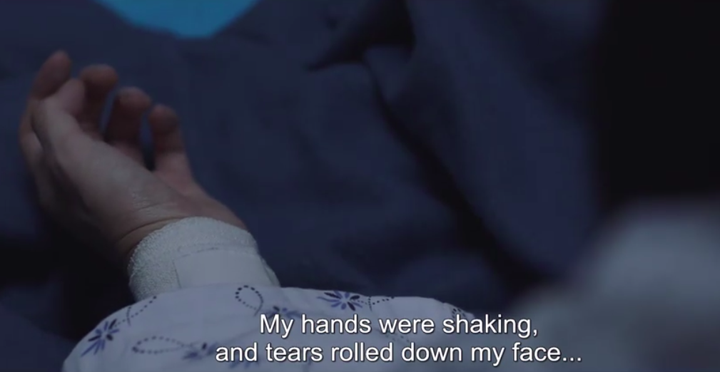 A close-up of Mi-jung's bandaged wrist. We can see she's wearing a hospital gown but the rest of the picture is out of focus. The subtitle reads 'My hands were shaking, and tears rolled down my face...'